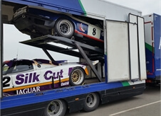 side view of an open covered car transport lorry showcasing two race cars within