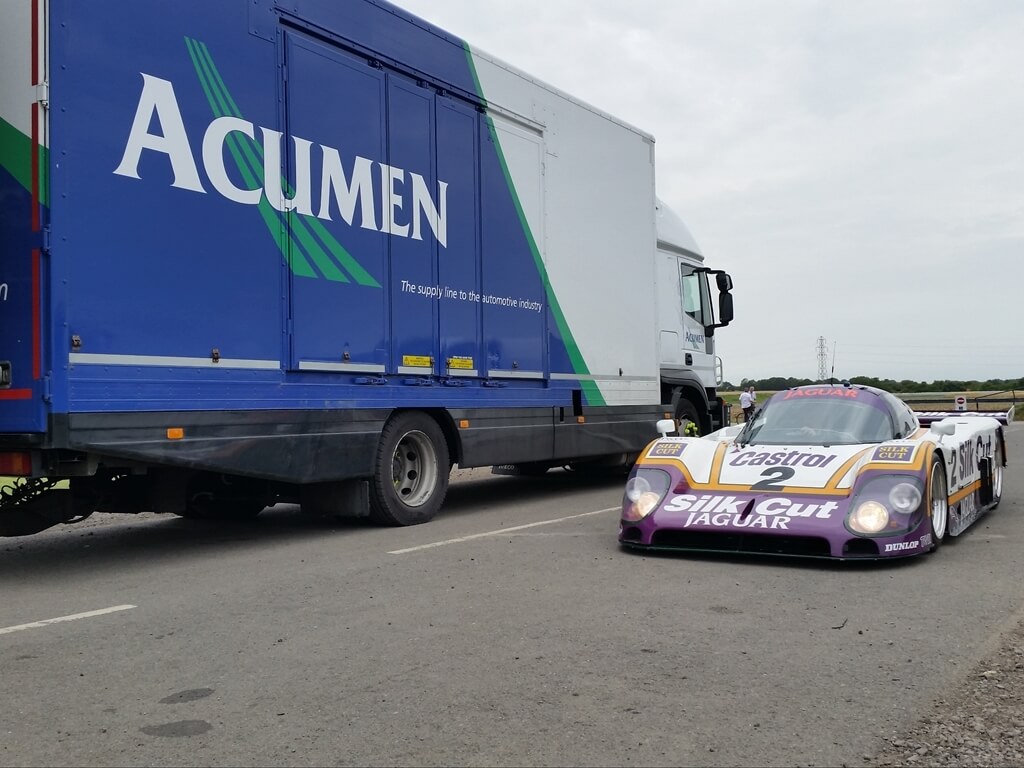 Acumen Logistics covered car transport lorry parked next to a race car that was delivered by the lorry.