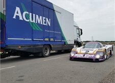 Acumen Logistics covered car transport lorry parked next to a race car that was delivered by the lorry.