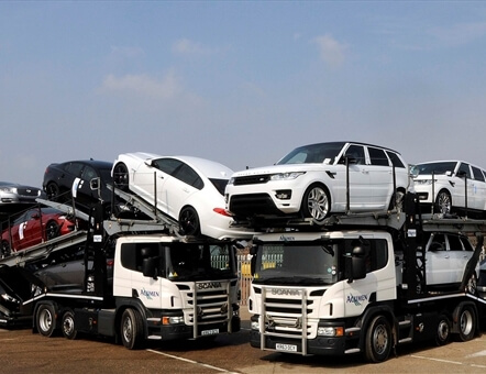 two Acumen Logistics car transporters parked next to each other with Range Rovers on one and Jaguars on the other.
